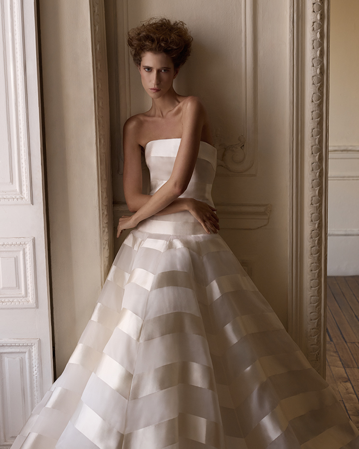 The veil becomes an extension of the narrative: long, weightless layers of tulle embroidered with scattered florals trail behind the bride, evoking memory, gesture, and passage. Each element is considered, each detail intentional—designed not to overwhelm, but to reveal.